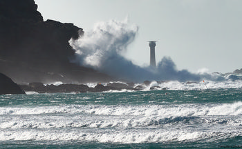 This landscape photograph captures the dramatic waves crashing against the Longships cliffs near Sennen Cove on the coast of Cornwall, United Kingdom, early in the afternoon during the winter season. The powerful sea surges and rugged cliffs are prominent, with the Longships Lighthouse standing tall as a key landmark in the background, highlighting the untamed nature of this coastal region. The turbulent ocean demonstrates the winter strength of the Atlantic, while the rocky shoreline and breaking waves showcase the natural beauty typical of Cornwall’s coastline. The lighthouse serves as a vital beacon for ships navigating these perilous waters, and the surrounding environment reflects the raw power and majesty of nature along the United Kingdom’s southwestern edge.